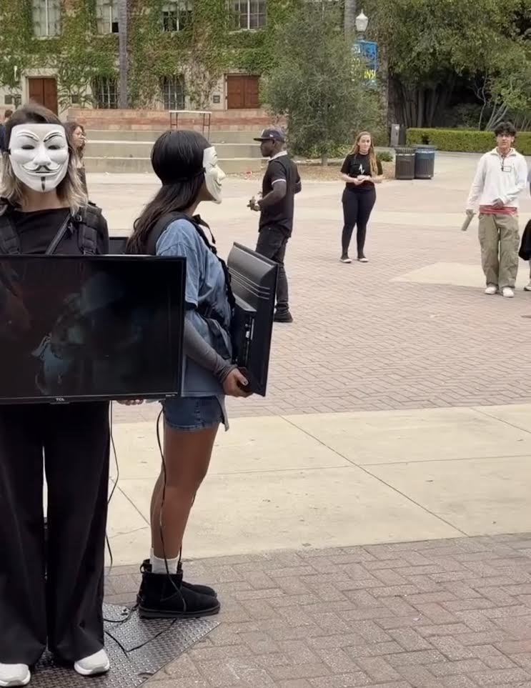 Activists in masks holding screens during a Cube of Truth on campus